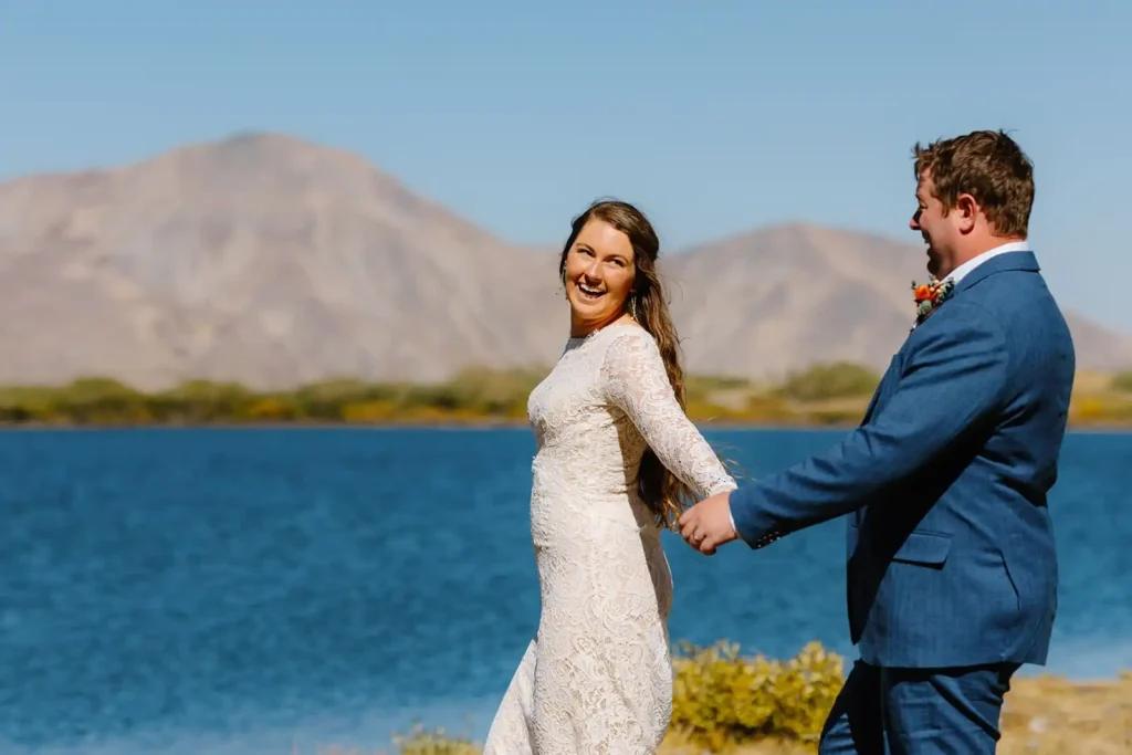 Candid, playful elopement couple runs together alongside alpine lake in the fall