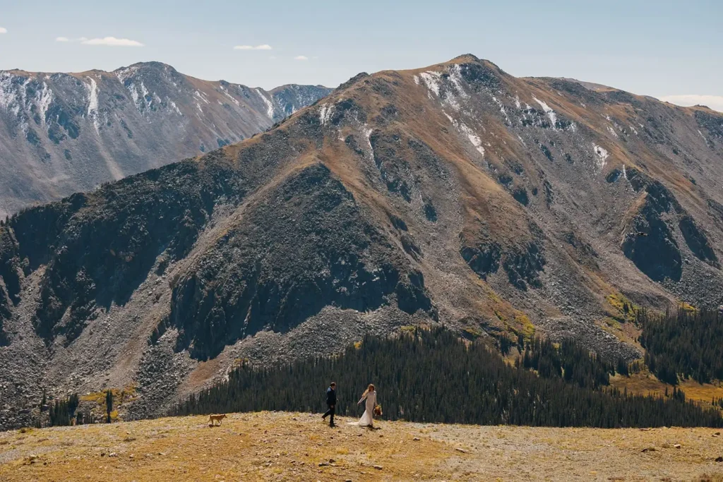 Adventurous couple hikes on their wedding day in Colorado. Scenic mountain view in the high rockies. Fall leaves color the surrounding landscape