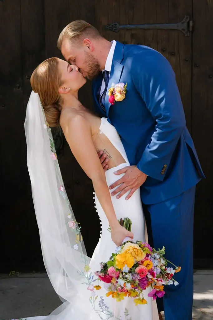 Bride and groom kissing featuring bright summer florals and an elegant veil. Inspiration for your summer Colorado wedding