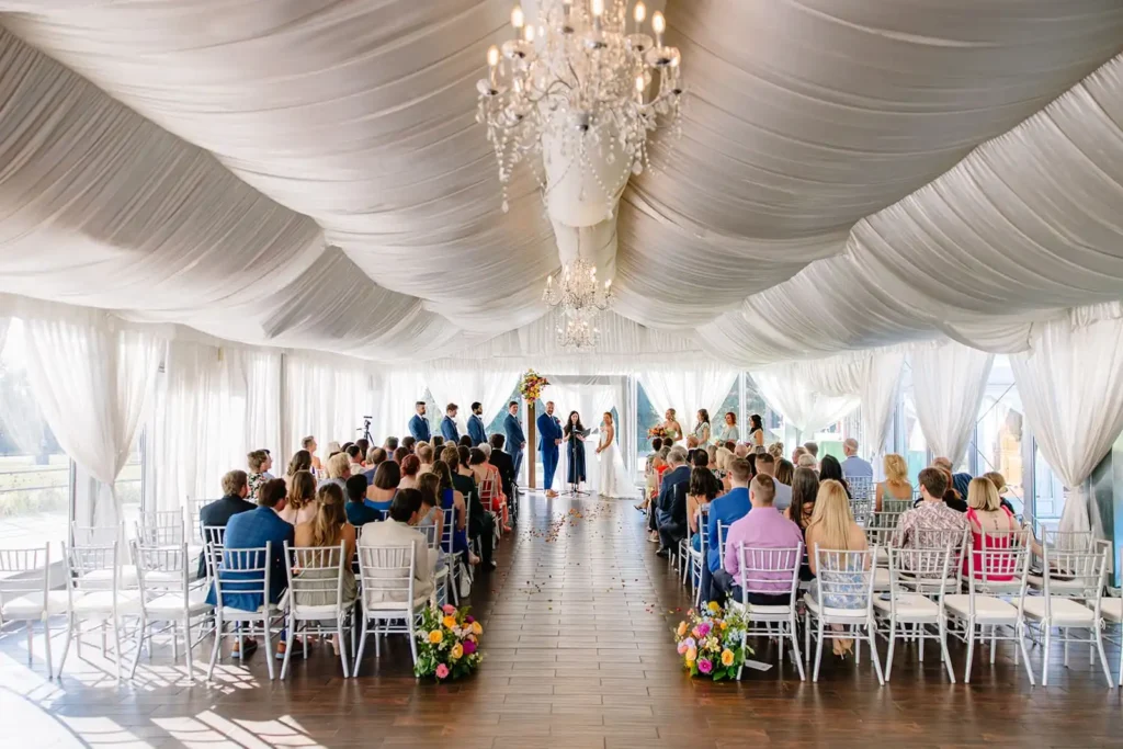 Leah Lach captures a beautiful indoor wedding ceremony at Wellshire Event Center featuring draping and chandeliers with bright flowers - a wedding photography shot list must-have