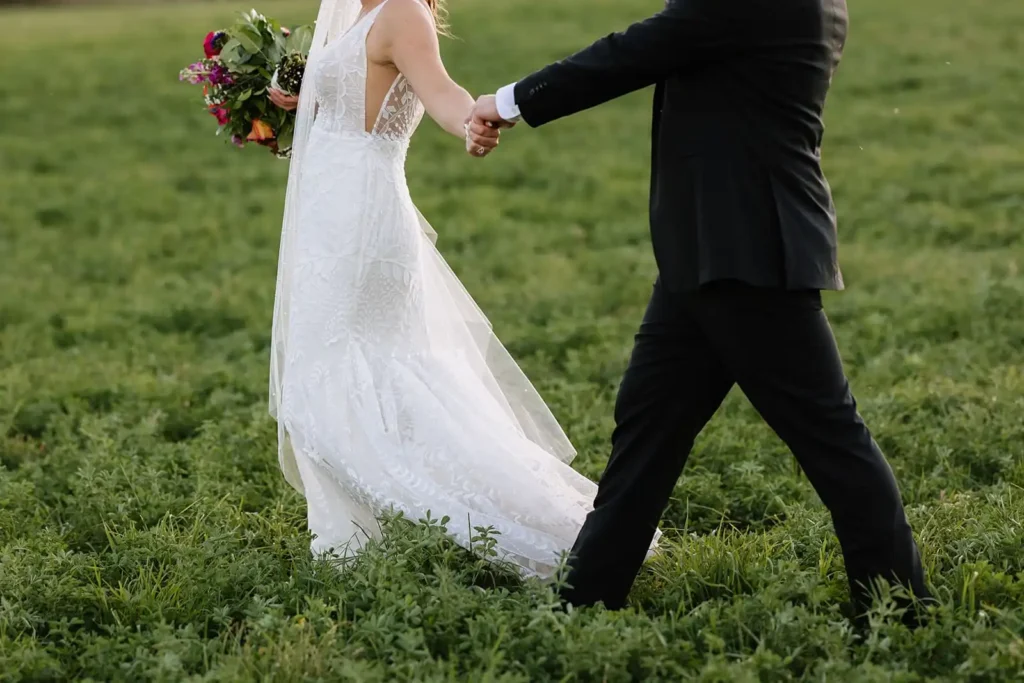 Bride and groom walking through a green field at sunset near Vista View Events wedding venue in Colorado.