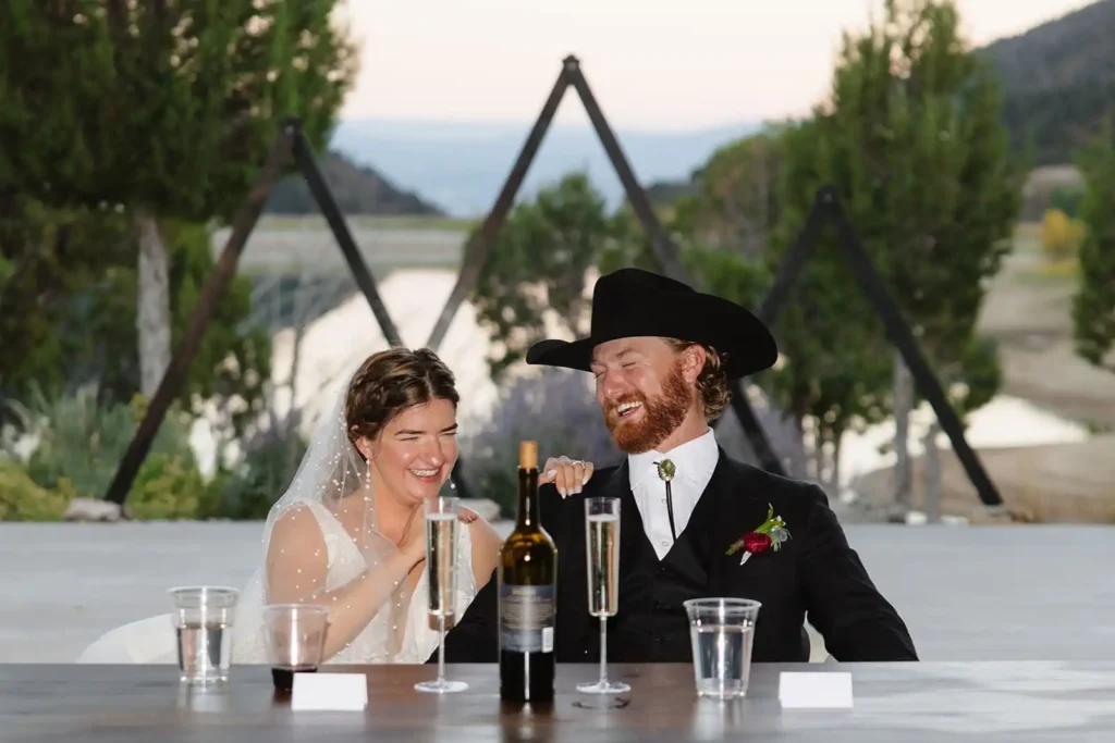Bride and groom laughing during reception toasts at Vista View Events with sun setting over the lake in the background.