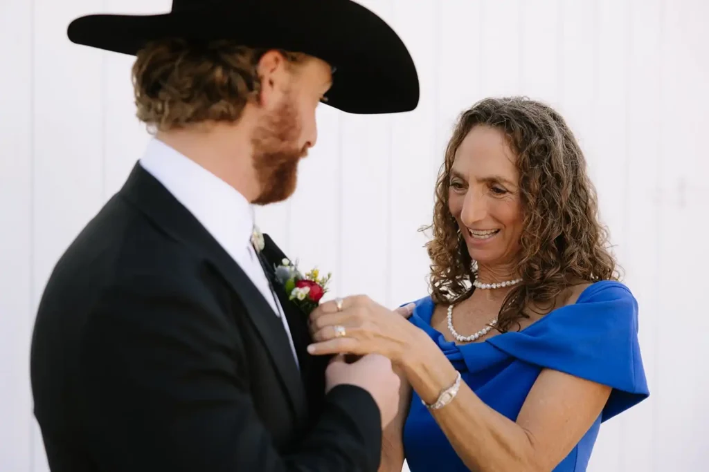 Candid moment of mother of the groom putting on the groom's boutonniere at Vista View Events Wedding