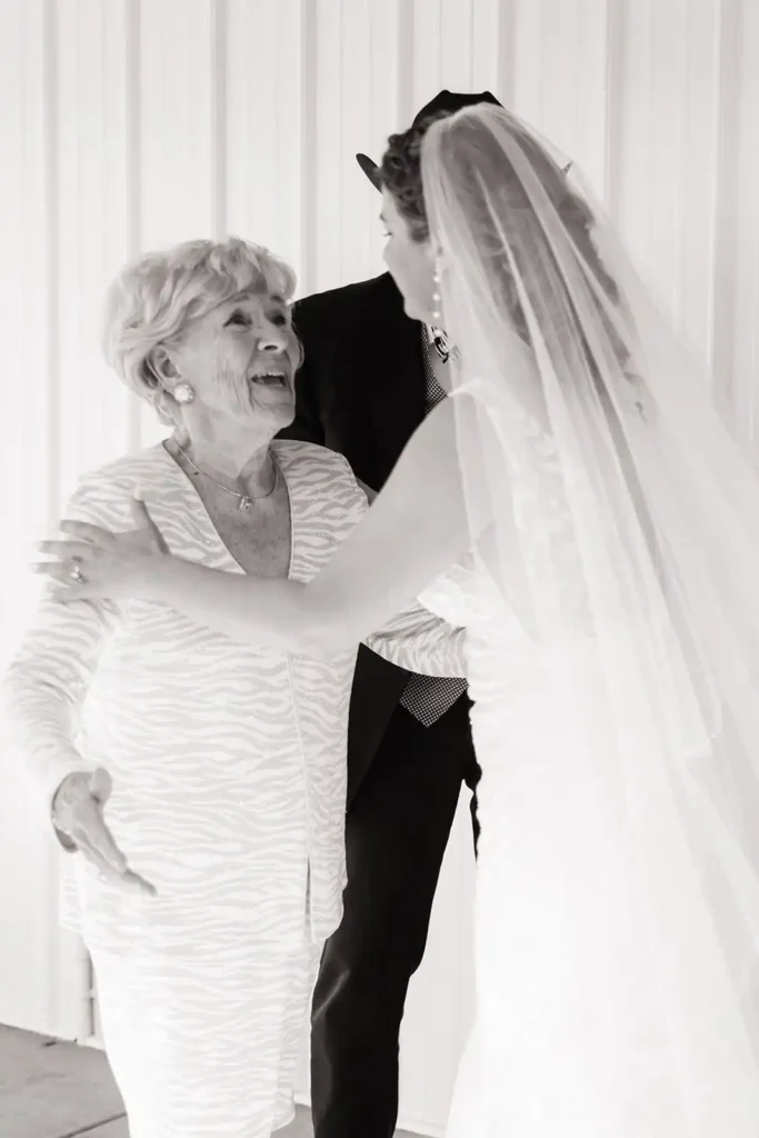 Bride and grandparents sharing an emotional first look in front of the white barn at Vista View Events wedding venue in Colorado.