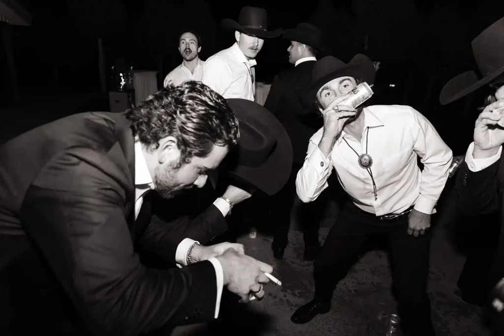 Groom and groomsmen laughing while shotgunning beers during rustic Colorado wedding reception.