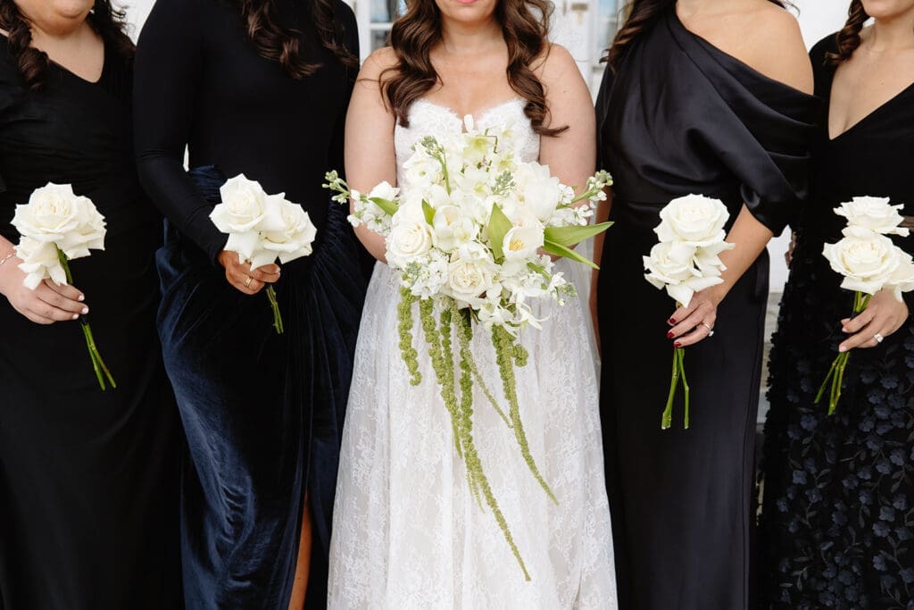 Bride posing with bridesmaids in black dresses holding white rose bouquets, clean and classic group portrait with timeless architecture near Denver.